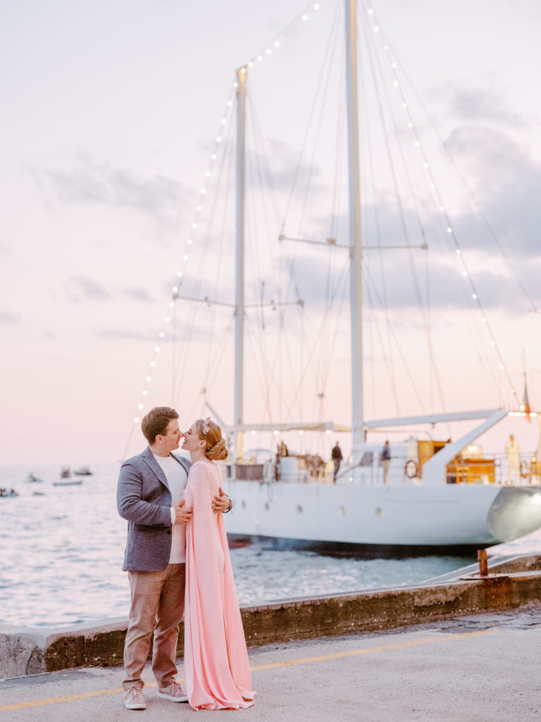 Couple kissing in front of a sailboat docked in the Amalfi Coast.