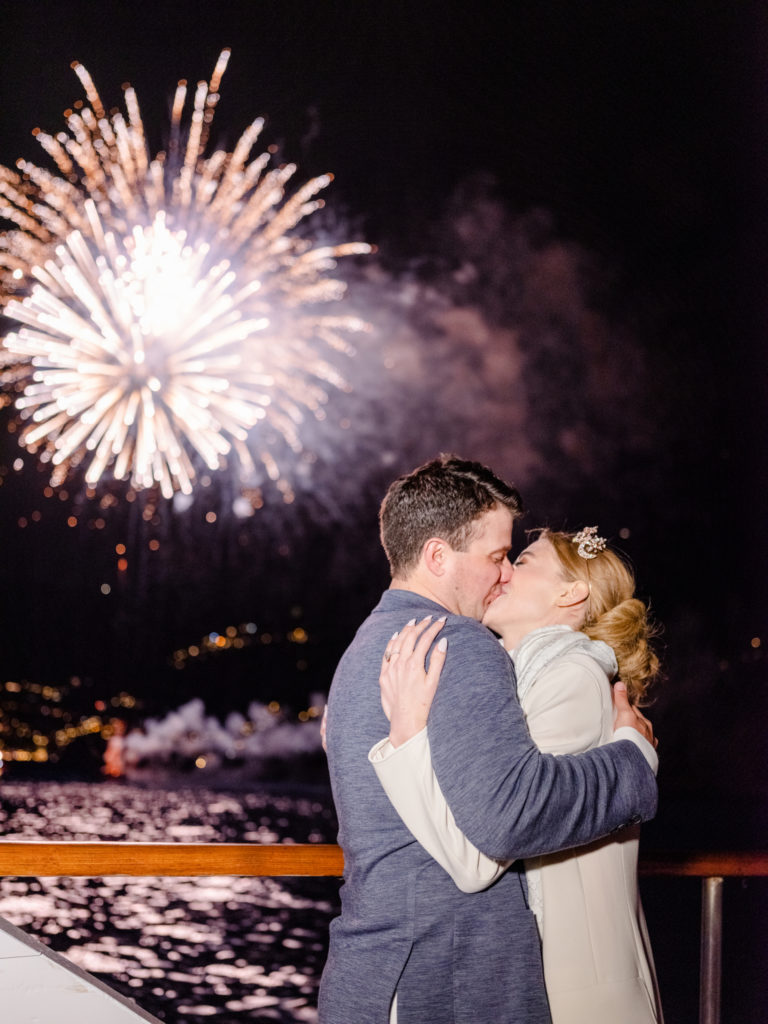 Couple kissing on a boat with fireworks in the background.