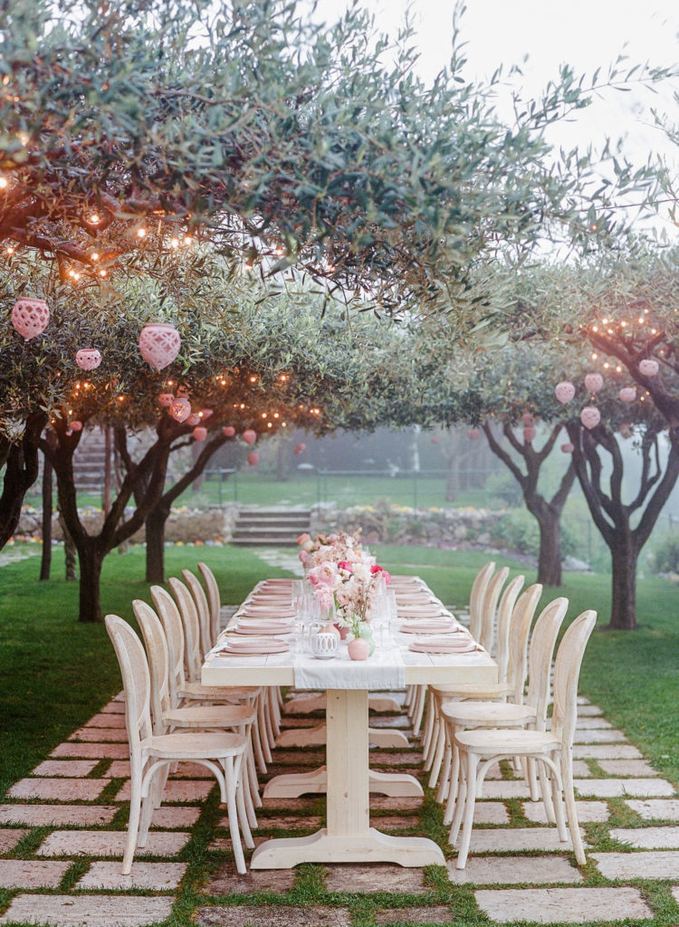 custom-tiled melon-inspired table with flowers under trees with hanging lanterns and twinkle lights