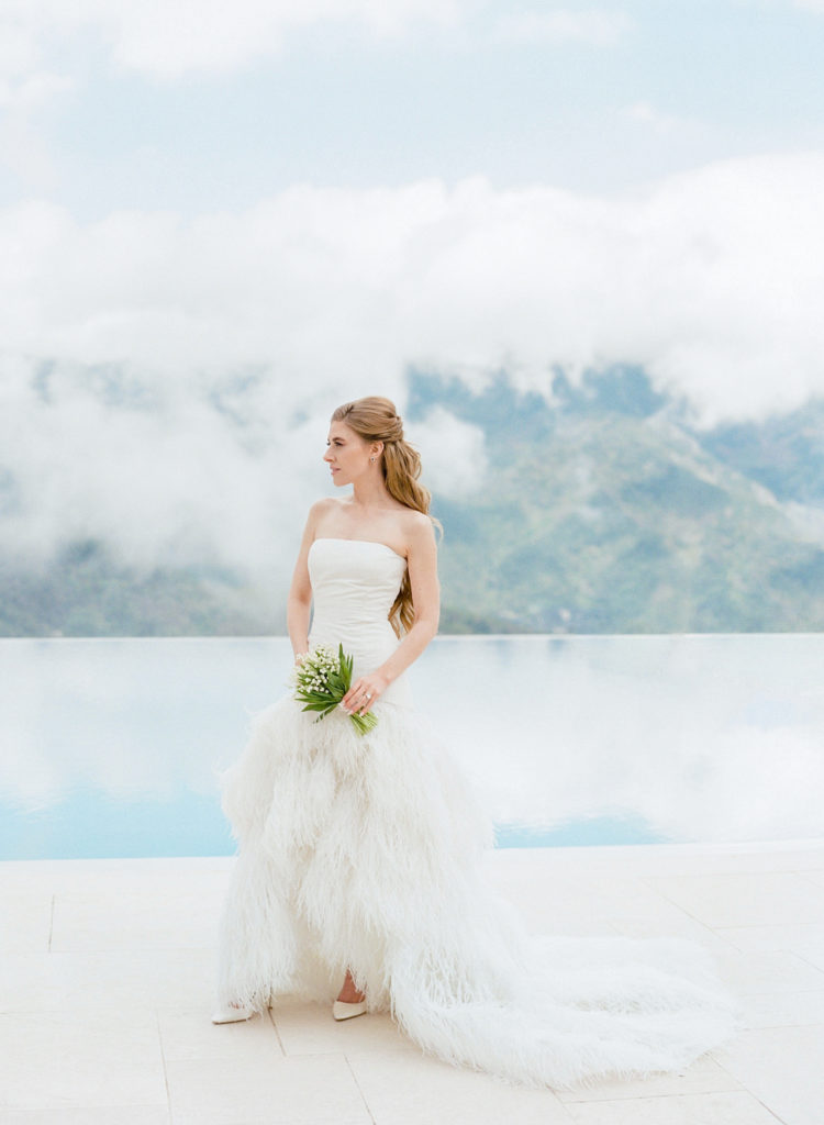 Bride wearing a white feathered wedding dress with the Amalfi Coast in the background